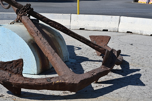 Close view on two old rusty anchors with chain placed in the middle of roundabout with traffic sign and concrete barrier in the city of Heraklion in Greece near the port.