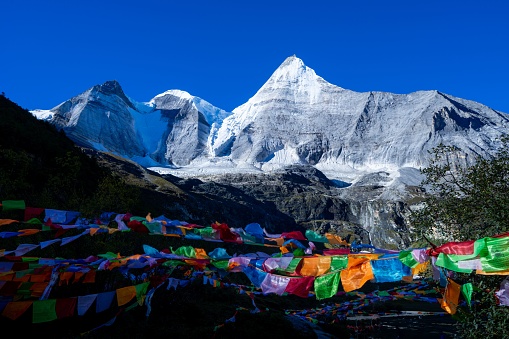 A landscape of snow-capped mountains featuring colorful Buddhist prayer flags, blowing in the wind