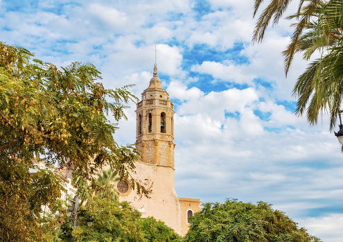Against a background of blue sky, palm trees and plants - view of the Church of St. Bartholomew and Santa Tecla in Sitges, Catalonia, Spain