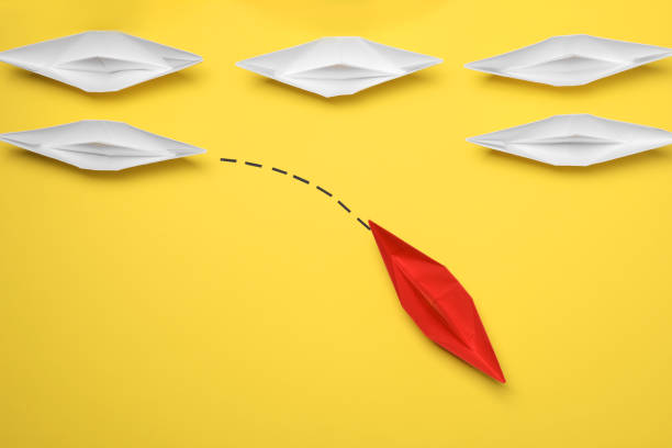 istock Red paper boat floating away from others on yellow background, flat lay. Uniqueness concept 1788119812