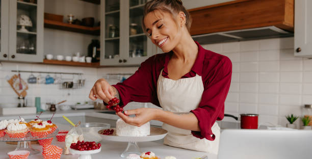 istock Happy female confectioner decorating cake with berries while standing at the domestic kitchen 1788134209
