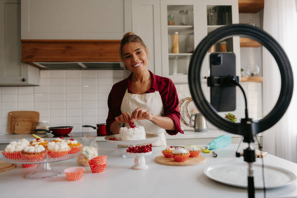 istock Happy female confectioner decorating cake on the kitchen while filming the process on smart phone 1788134219