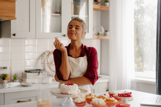 istock Joyful young female confectioner enjoying marshmallow while decorating cake at the kitchen 1788144775