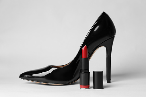 Beautiful red lipstick and black high heeled shoe on white background
