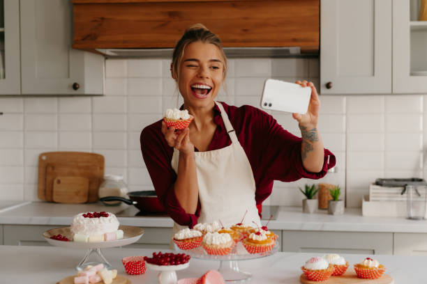 istock Joyful female baker using smart phone while making selfie with various cakes and muffins laying on the table 1788152202