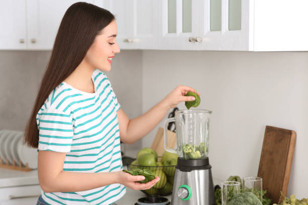 istock Young woman adding spinach leaves into blender with ingredients for smoothie in kitchen 1788157367