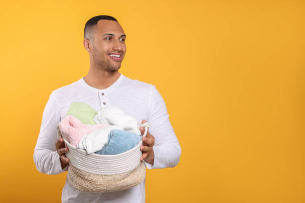 istock Happy man with basket full of laundry on orange background. Space for text 1788180593