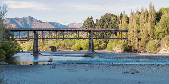 Old Lower Shotover Bridge, a historical bridge in Queenstown, New Zealand, arching over a serene river with a backdrop of mountains and trees. Part of the Queenstown trails.