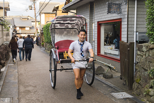 Kyoto, Japan - April 16, 2023: unidentified Japanese rickshaw driver in an alley in Kyoto. By 1872 it was the main mode of transportation in Japan, today it is a tourist attraction
