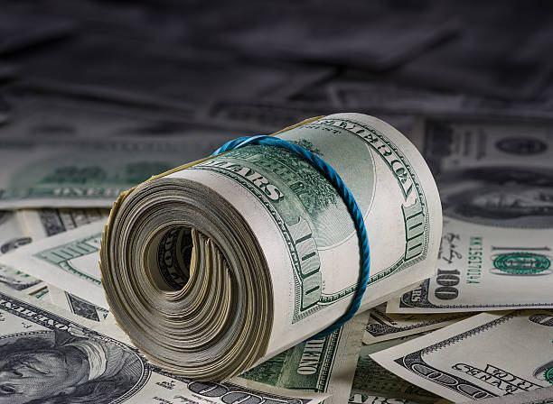 istock Roll of hundred dollar bills over a surface of more bills 178824866
