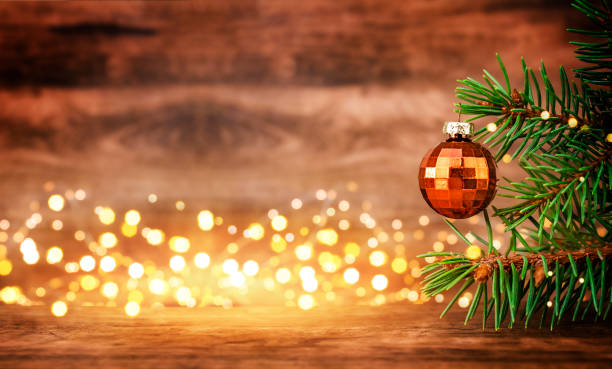 Christmas Fir tree with Golden Bauble on wooden table and defocused lights in the background. Copy Space