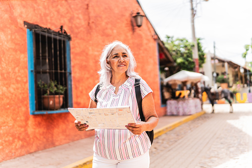 Senior tourist woman using a map while walking through the tourist town