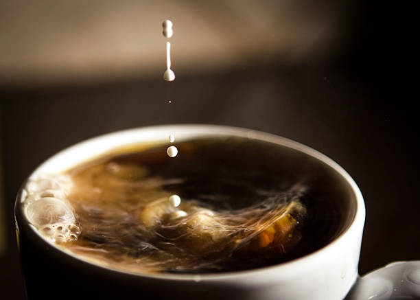 Cream is poured into a cup of hot coffee with droplets splashing around.