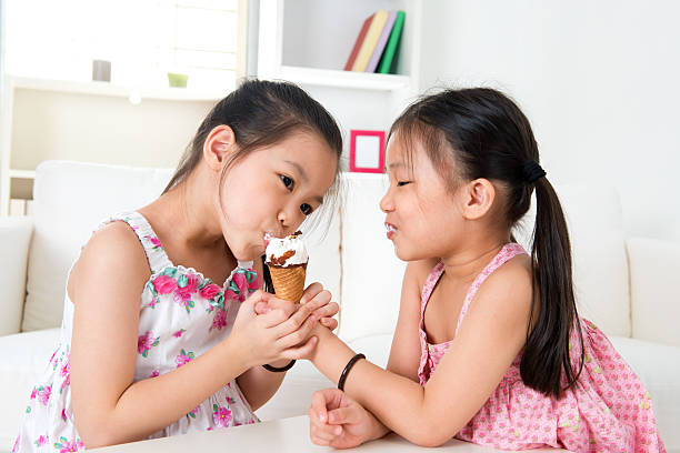 Asian girls eating ice cream Eating ice cream. Asian girls sharing an ice cream. Beautiful children model at home. asian little chinese girls eating ice cream stock pictures, royalty-free photos & images