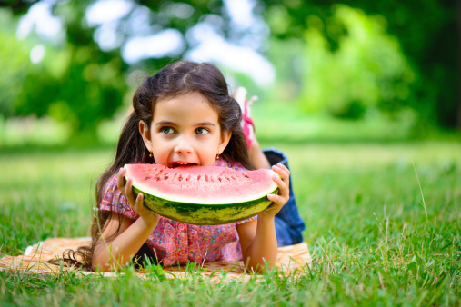Cute hispanic girl eating watermelon at park