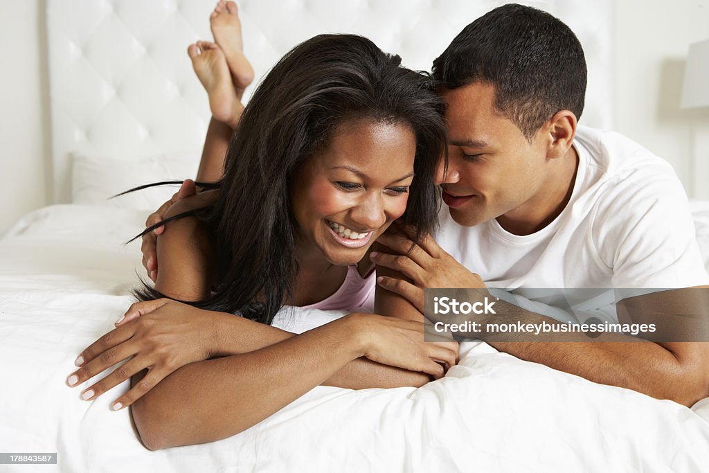 Couple smiling wearing white relaxing on a white bed Couple Relaxing In Bed Wearing Pajamas Lying Down Snuggling Cozy Stock Photo