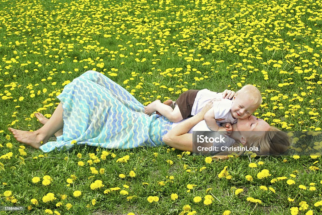 Mother Kissing Baby in Dandelion Field A young, attractive mother, laying in a field of dandelions, kissing her baby boy. Family Stock Photo