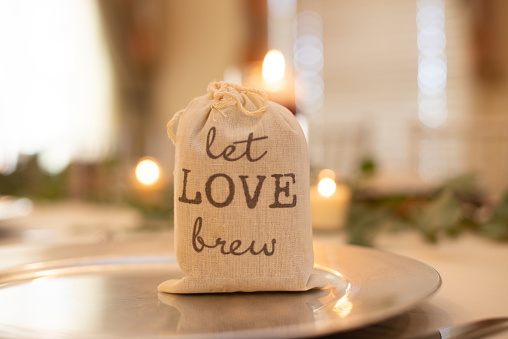 Canvass bag that reads let Love Brew wedding center piece filled with cofee grinds on dinner table