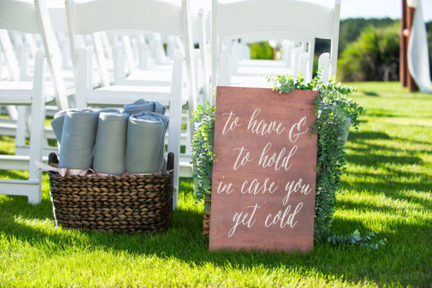 panneau de bois qui se lit à avoir et à tenir au cas où vous auriez froid sur l’herbe lors de la cérémonie de mariage devant des chaises blanches à côté d’un panier en osier avec des serviettes plus proches - furniture store furniture retail textile photos et images de collection