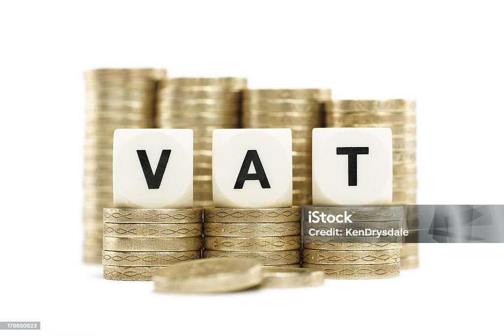 VAT (Value Added Tax) on Stacked Coins with White Background The letters VAT (Value Added Tax) on lettered dice on stacks of gold coins on a white background. British Coin Stock Photo