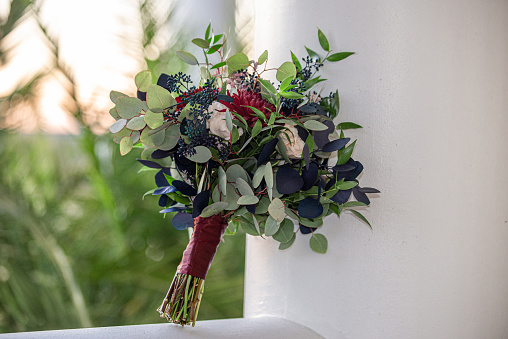 wimsical red,pink and white bouquet with blue and green leaves outdoors on pedistal