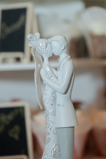 Bride and groom passionately kissing ceramic cake toppers on top of cake and infromt of out of focus cup cakes