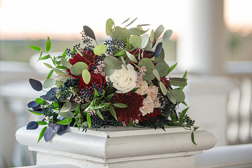 Majestic red,pink and white bouquet with blue and green leaves outdoors on pedistal