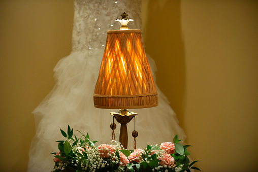 Warm antique lamp on table with roses ans wedding dress in background bride getting ready