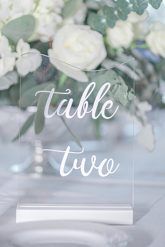 Fancy glass table number that reads Table Two on whhite table in front of bouquet of white roses