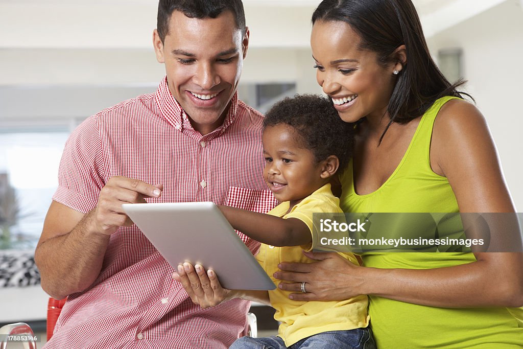Man, woman, and child using a tablet in a white room Family Using Digital Tablet In Kitchen Together Sitting Down Smiling Family Stock Photo