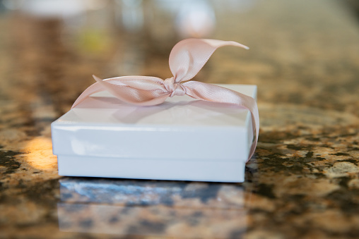 Small romantic white gift box wrapped in a pink bow with lace on counter top
