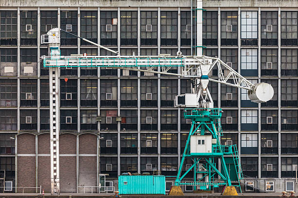 Old green harbor crane in front of an ancient factory