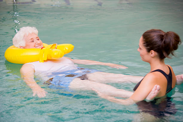 Instructor And Elderly Patient Undergoing Water Therapy Instructor And Elderly Patient Undergoing Water Therapy With Inflatable Looking At Each Other hydrotherapy stock pictures, royalty-free photos & images