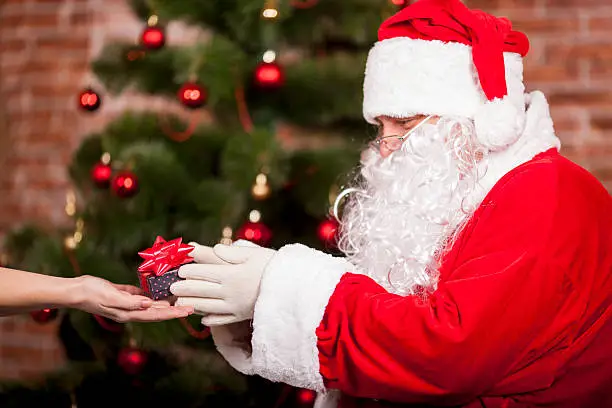 Santa Claus gives a Christmas present at the tree