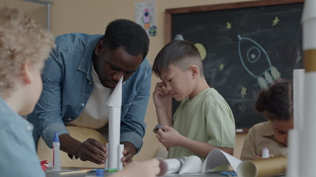 Elementary School Student Making Paper Rockets with Teacher