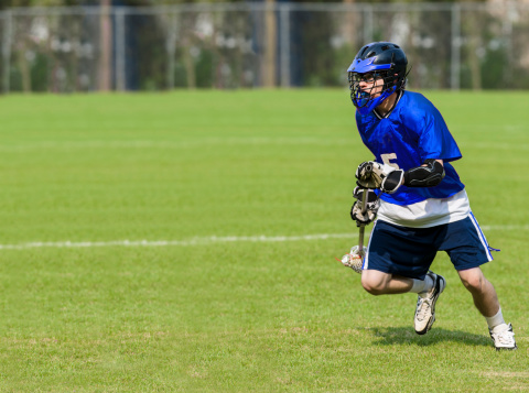 Male lacrosse player with goggles and mouthguard preparing to attack on a grass field with copy space