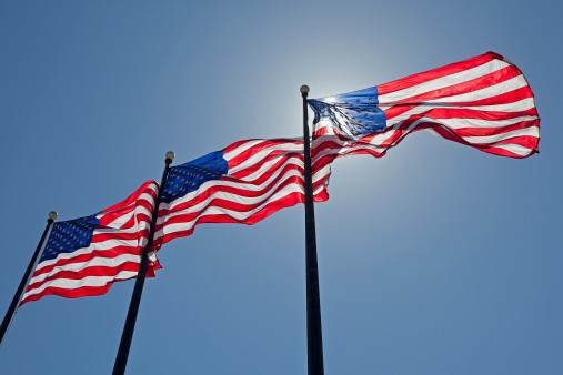 Three United States of America Flags are Blowing in the Wind in front of the Sun.