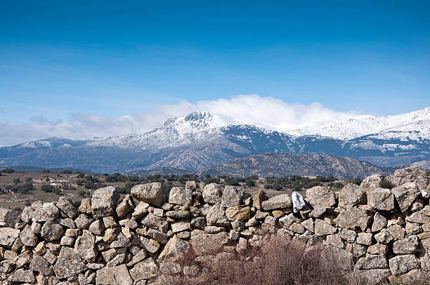 Stone wall. At the background, snow capped peaks of the Guadarrama Mountains. Photo taken in Colmenar Viejo, Madrid Province, Spain juniperus oxycedrus stock pictures, royalty-free photos & images