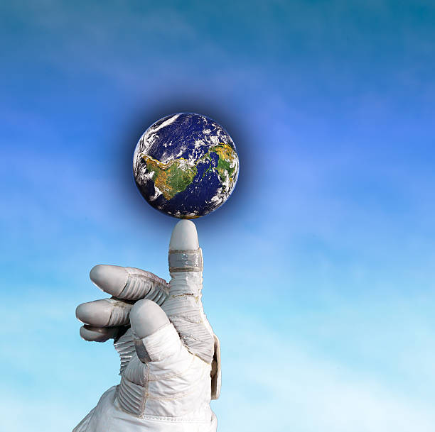Hand of an astronaut holding the globe on his finger on blue sky background.