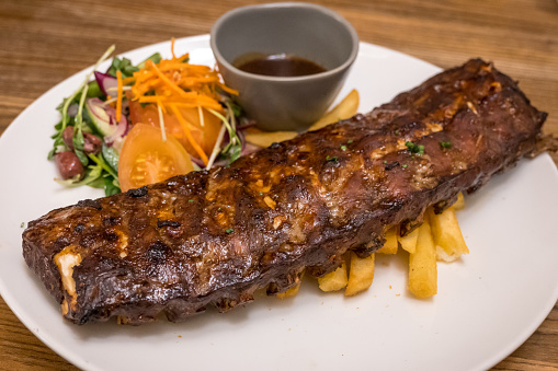 Grilled juicy barbecue pork ribs in a white plate with fries and salad