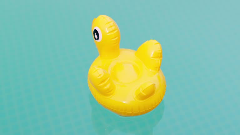 Inflatable yellow duck toy swims in swimming pool of clear blue water on a bright sunny day