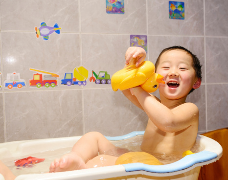 young Asian baby boy holding  a yellow plastic duck in bath