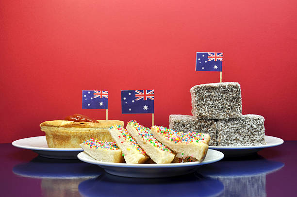 Celebrate with traditional Aussie tucker food Plate of traditional Aussie tucker, meat pie and sauce, fairy bread and lamingtons, with Australian flag against a red and blue background, for Australia Day January 26, Anzac Day April 15, or Australian holidays or events. downunder stock pictures, royalty-free photos & images