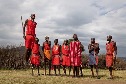 Nairobi, Kenya – July 10, 2022: A cheerful African man standing on one leg while balancing a stick in front of a group of people