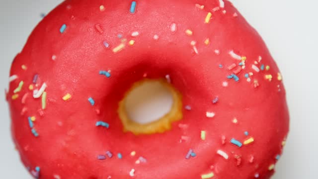 Strawberry donut with colored sprinkles rotating as approaches at light background top view.