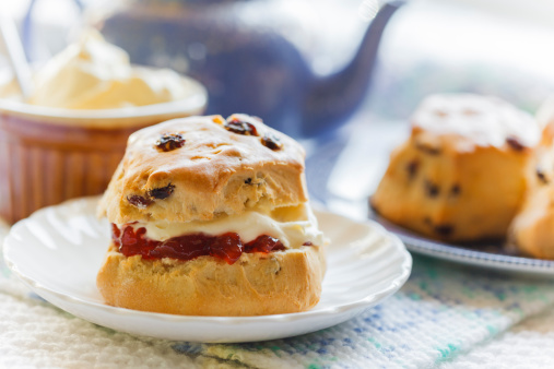 Traditional afternoon tea with scones, jam and cream, blue teapot and crockery, on textured background,  light and summery teashop menu