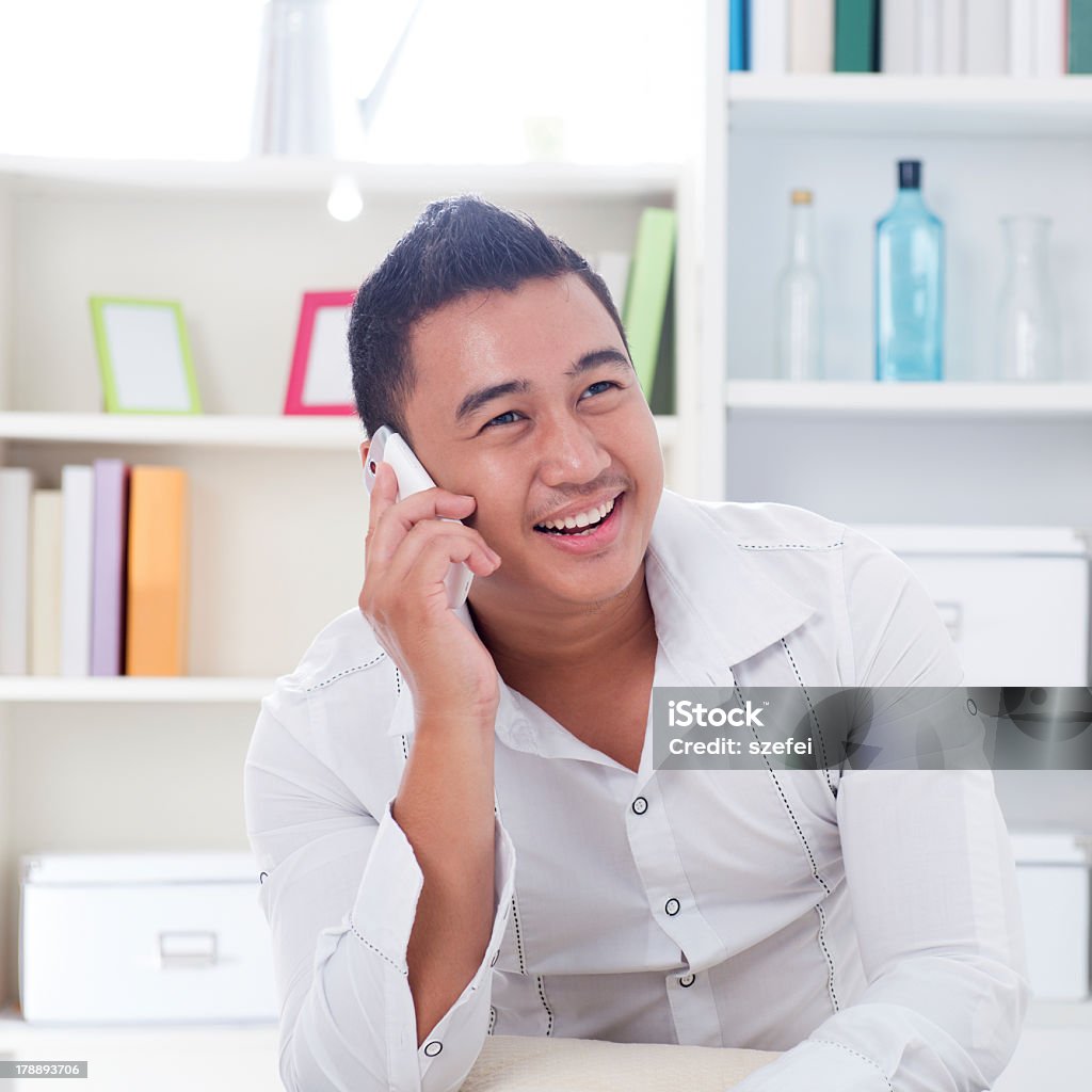 Smiling young man in white shirt taking on a phone Young Asian man talking on the phone. Lifestyle Southeast Asian man at home. Handsome Asian male model. Adult Stock Photo