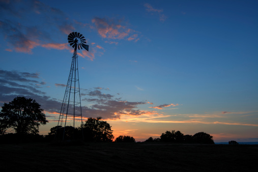 A country windmill silhouetted in the sky as the sun sets in the distance.