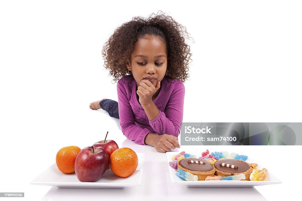 Piccola ragazza asiatica africana esitazione tra frutta o dolciumi - Foto stock royalty-free di Scegliere