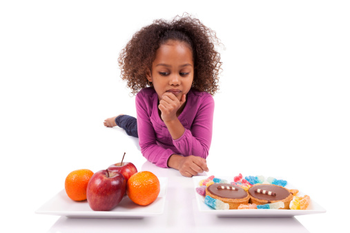 Little African Asian girl hesitating between fruits or  candy